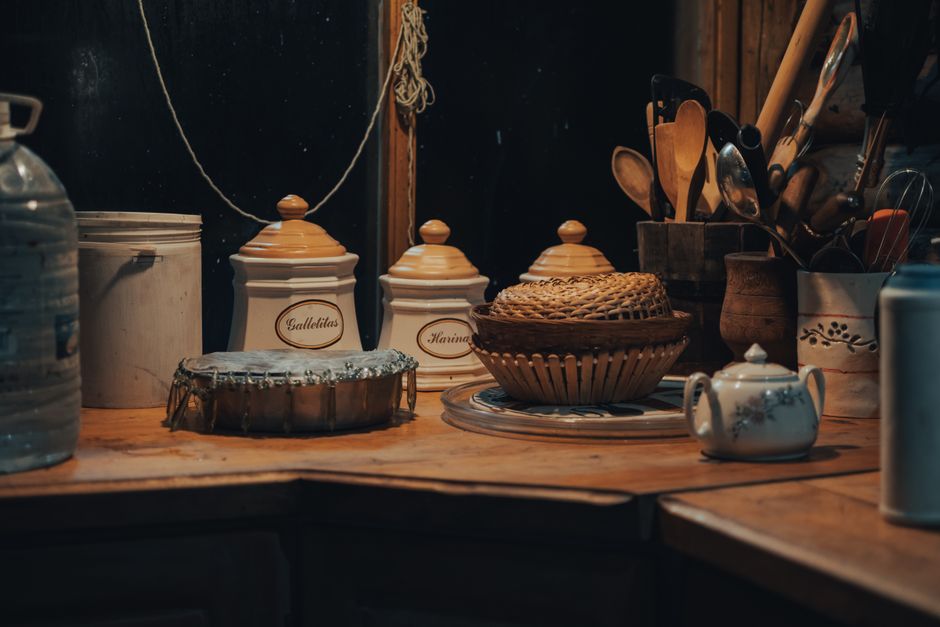 Cozy kitchen scene featuring wooden utensils, a teapot, and storage jars with warm lighting.